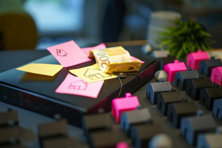Euro banknotes on laptop with sticky notes and house models, symbolizing real estate investment.